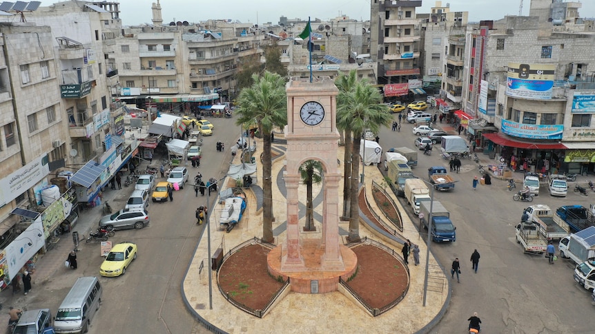 Aerial view of ornate clocktower and plaza with palm trees, in the middle of two streets