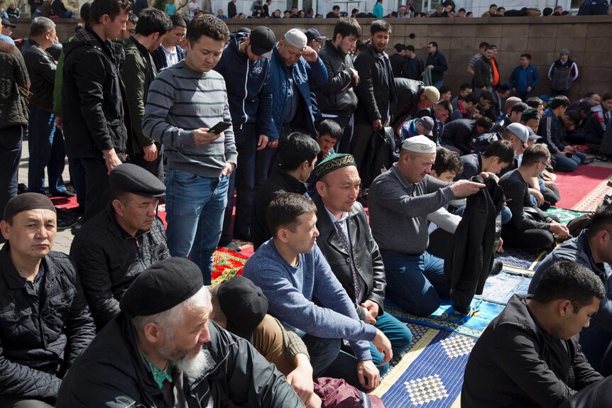 Omir Bekalic, centre, kneels on the ground and is surrounded by a crowd of people.