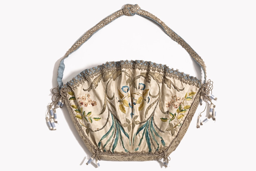 An embroidered bag-like object consisting of a large tasselled pocket on a cord.