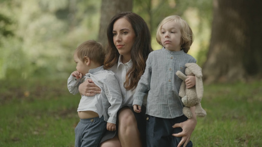 A woman kneels in a forest holding two small boys