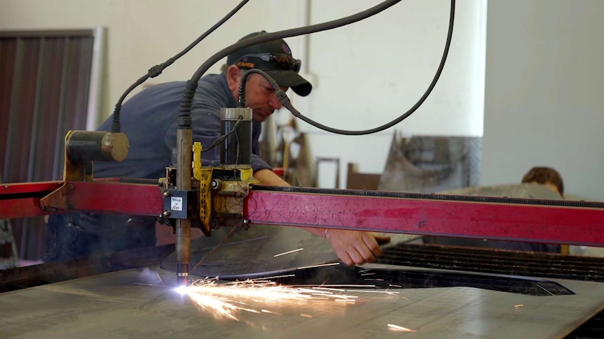 A man uses a laser cutter on metal in a workshop