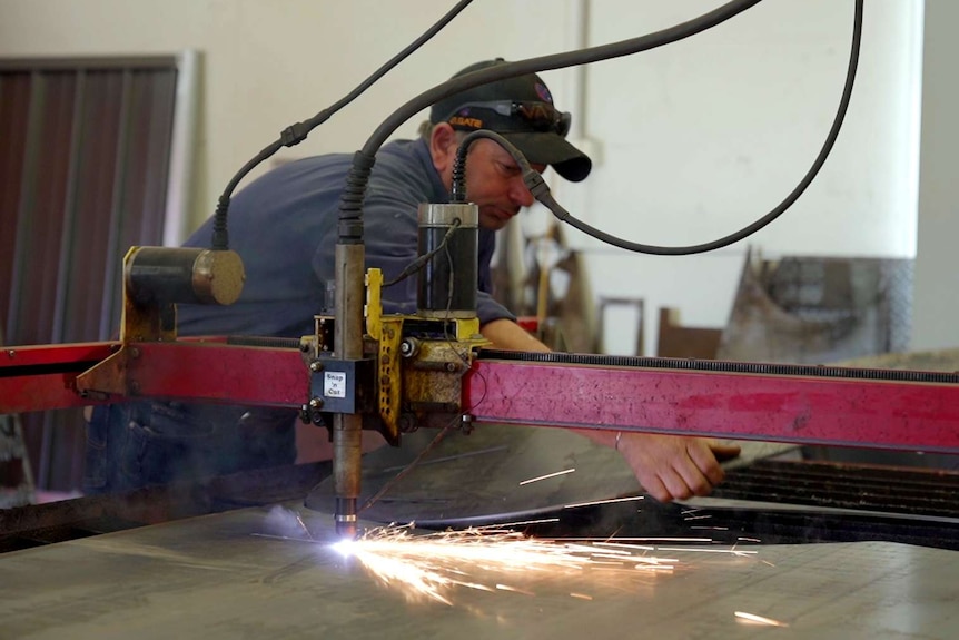 A man uses a laser cutter on metal in a workshop