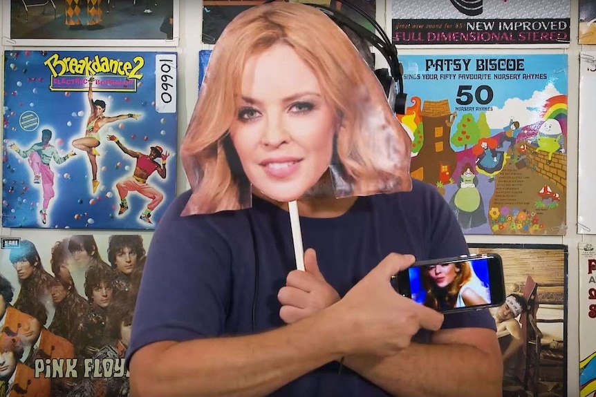 A man holds up a Kylie Minogue mask.