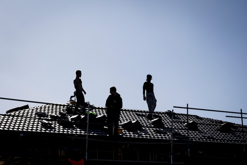 Three men standing on the roof of an unfinished house.