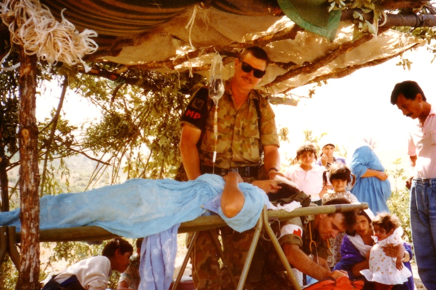 Two Australia soldiers under a temporary shelter medically attending to refugees in Iraq.