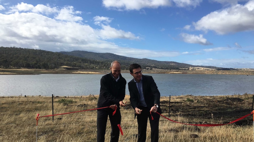 two ministers cut a ribbon in front of a dam