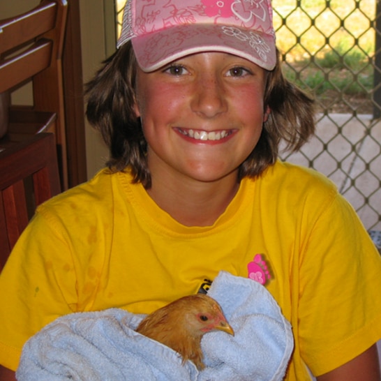 A young girl wearing a pink cap is holding a chicken wrapped in a towel 