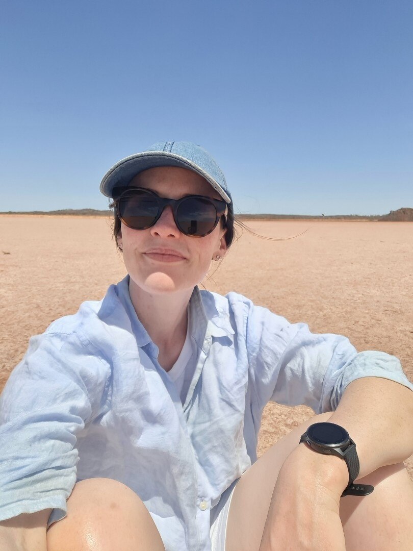 A woman in a cap and sunglasses sitting outdoors during a sunny day