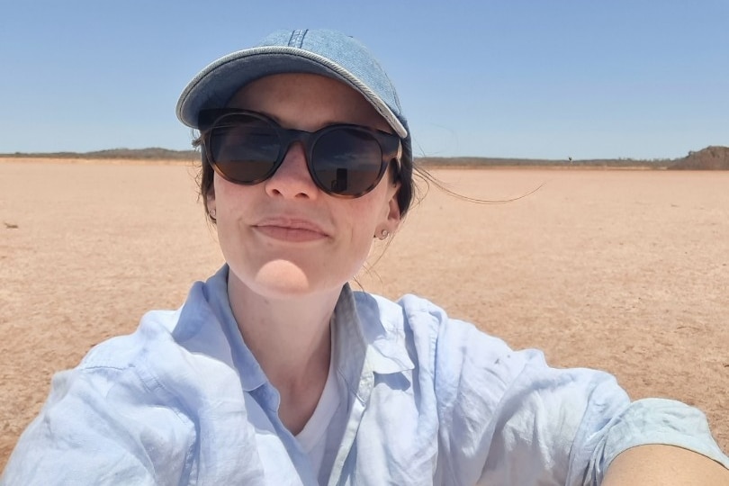 A woman in a cap and sunglasses sitting outdoors during a sunny day