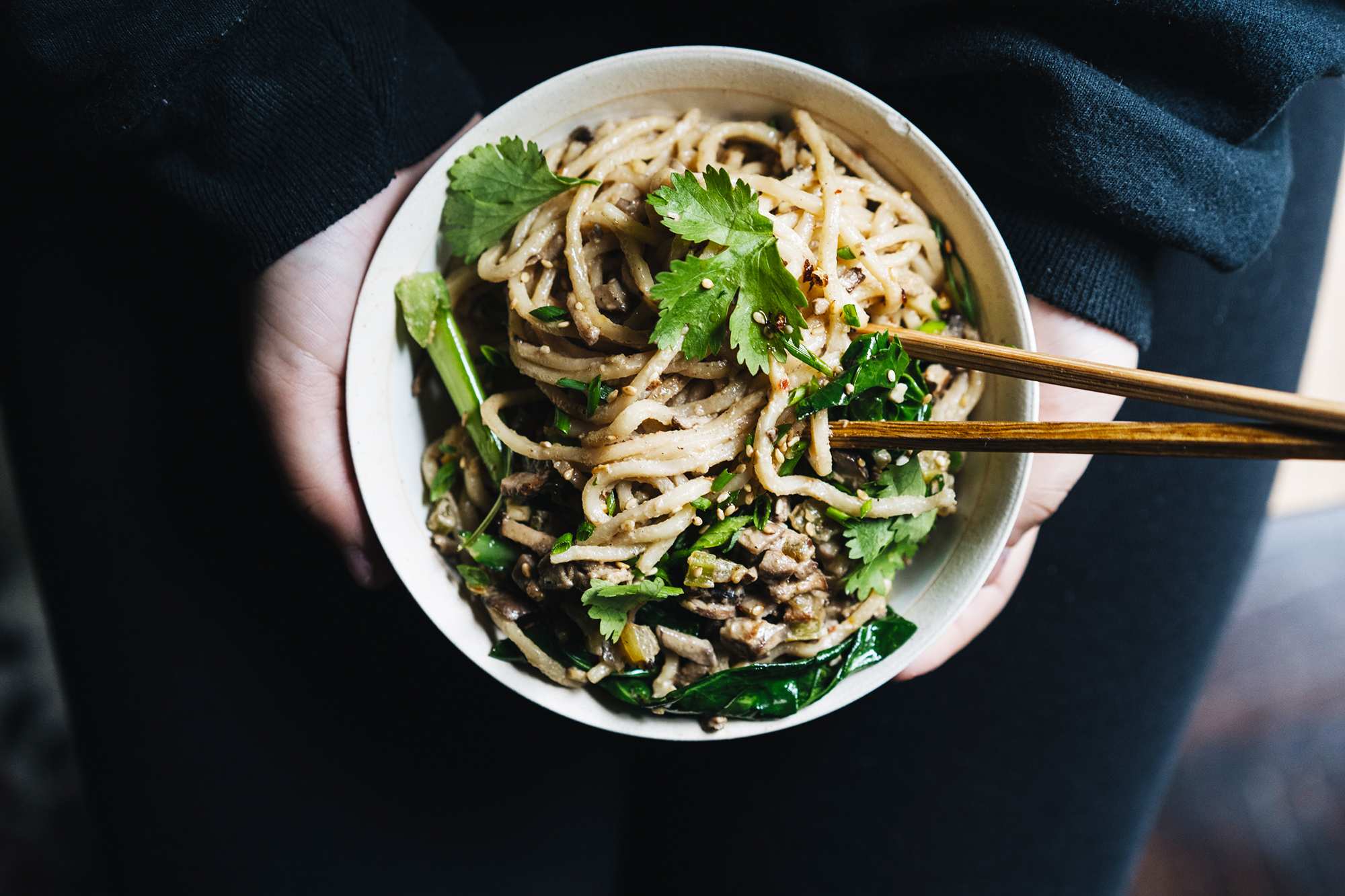 A person holds a bowl of Chinese noodles topped with sesame seeds, mushrooms and Chinese broccoli, for a Lunar New Year meal.