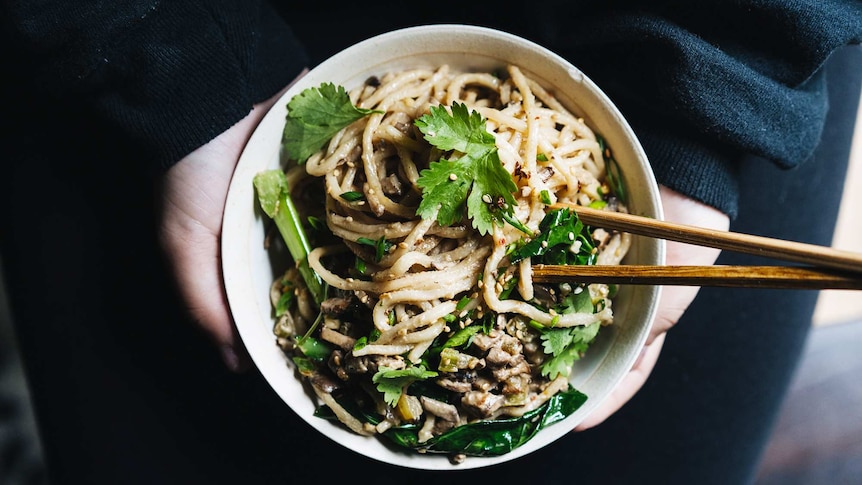 A person holds a bowl of Chinese noodles topped with sesame seeds, mushrooms and Chinese broccoli, for a Lunar New Year meal.