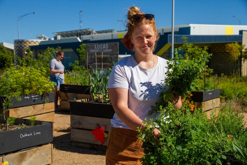 A woman holding a punch of herbs stands in the middle of a vegetable garden.