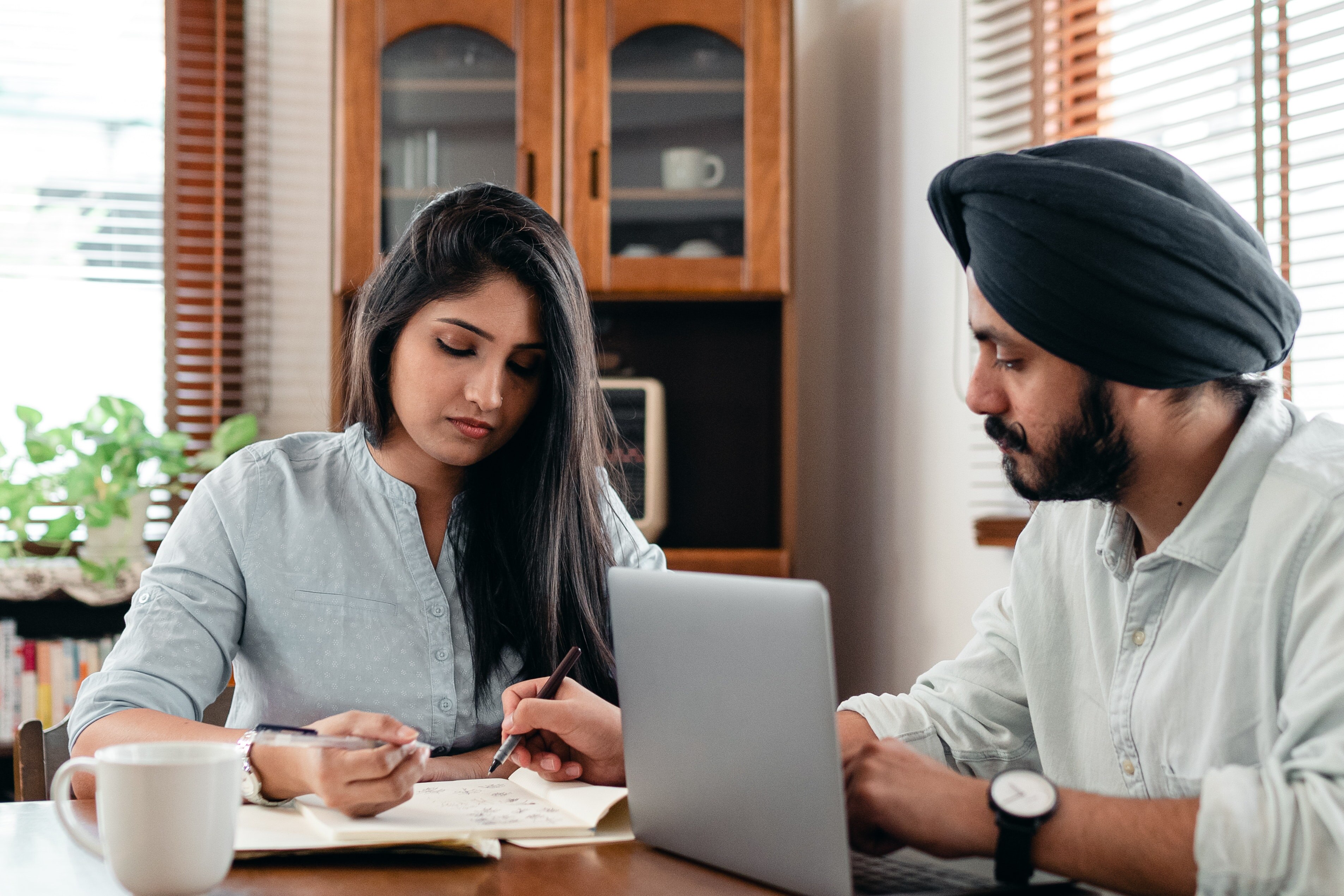 A couple holding pens look at documents while sitting at a kitchen table, in a story about stop putting off making a will.