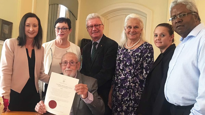 Ken Blanch (seated) holds the Royal Pardon for Kipper Billy, with six people standing behind him.