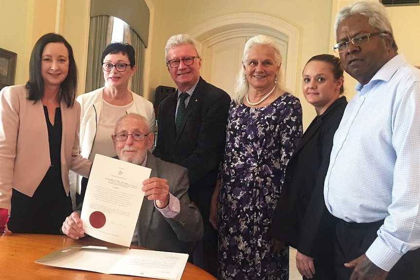 Ken Blanch (seated) holds the Royal Pardon for Kipper Billy, with six people standing behind him.