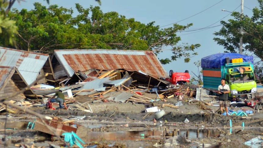 A man stands amid water and debris caused by a tsunami in Palu