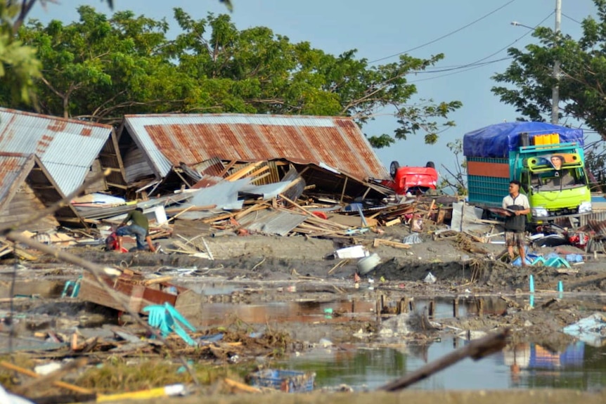 A man stands amid water and debris caused by a tsunami in Palu