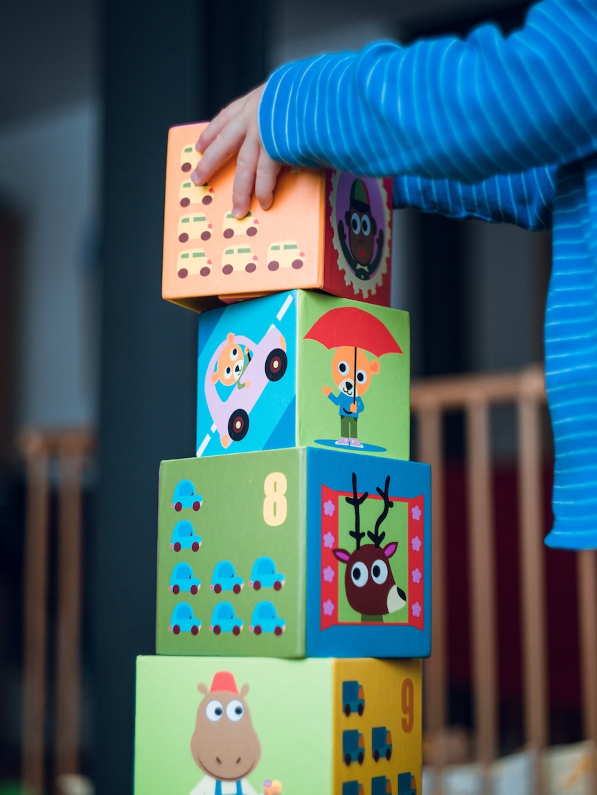 A small child stacks blocks high into a tower.