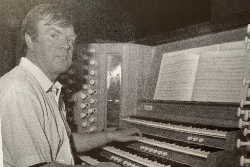 A black and white shot of a man sitting at an organ.