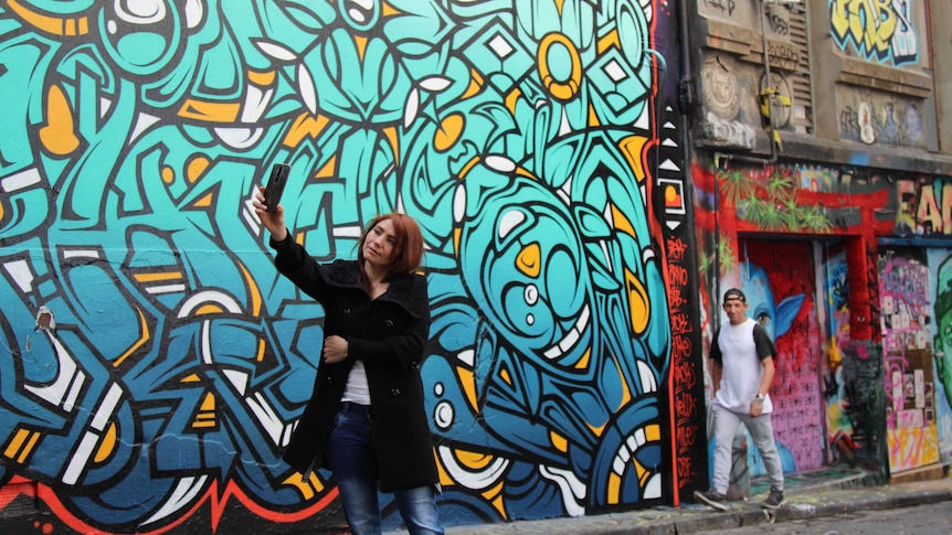 Woman takes a selfie photo on her phone in front of colourful street art.