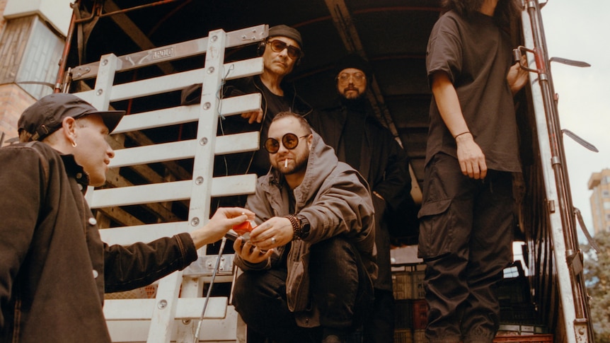 the five members of Unknown Mortal Orchestra sit in a wooden stairwell of a bodega