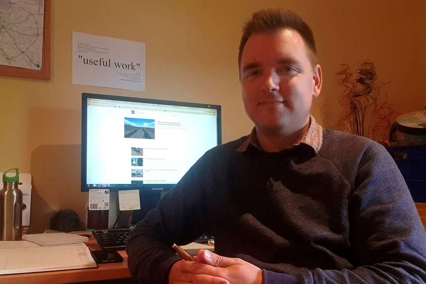 A man sits in front of a computer screen in a room.