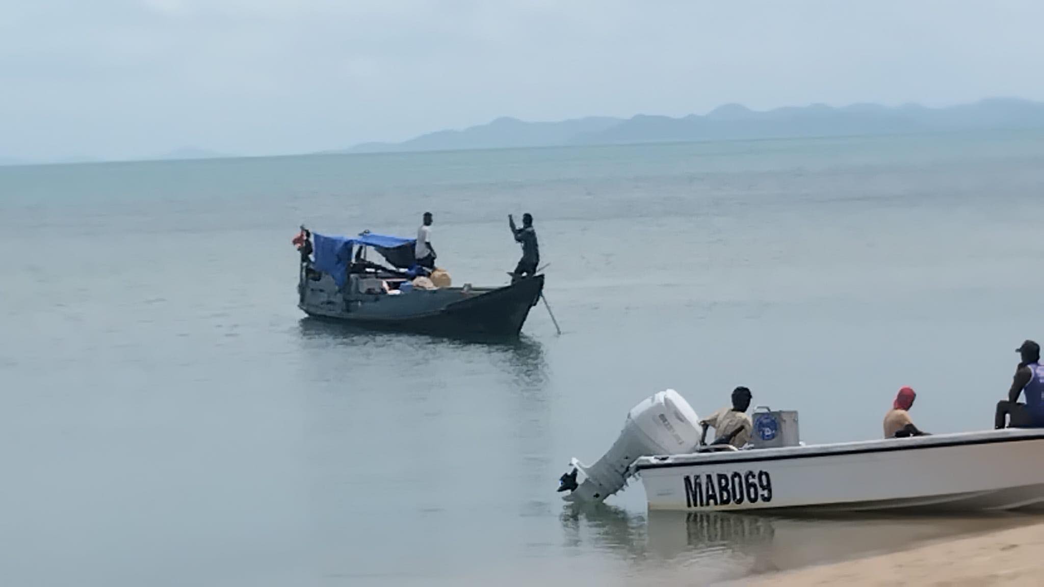 Vários pequenos barcos de pesca e pessoas na praia de uma ilha tropical.
