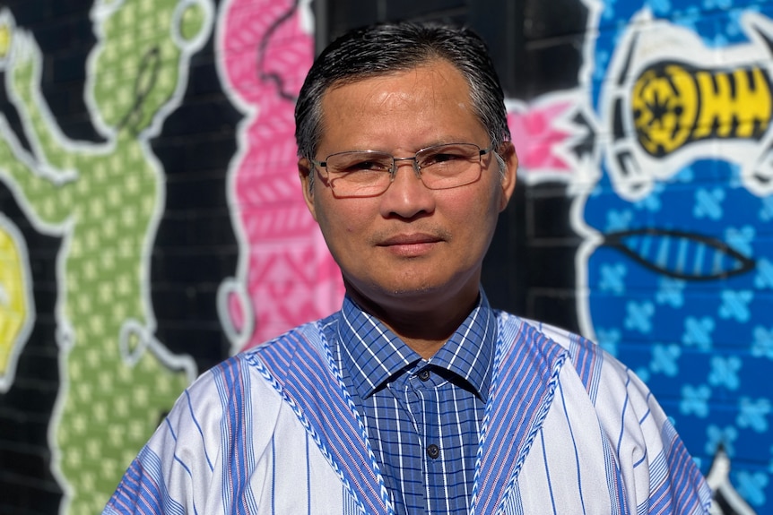 Karen man standing in front of colourful mural painted on a building wall