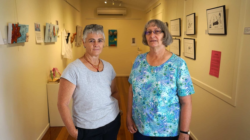 Artists Faye Cook and Jan Sody stand in a gallery surrounded by their works.