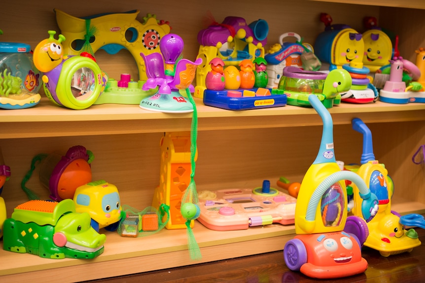 Brightly coloured plastic children's toys on a wooden bookshelf at the Darwin Toy Library.