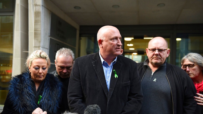 The Dunn family stand before a row of microphones while each wear a green lapel ribbon.