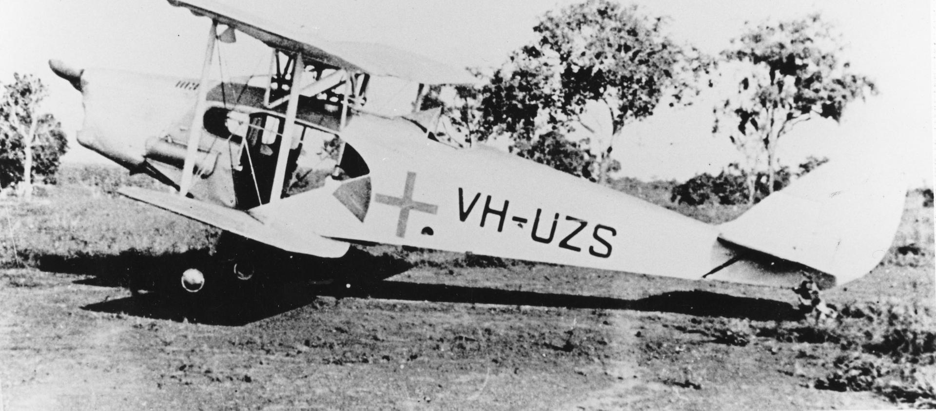 An old plane with a cross on it is landed in the bush.  The photo is old and in black and white. 