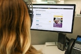 Woman sits in an office with headphones on looking at an Optus webpage