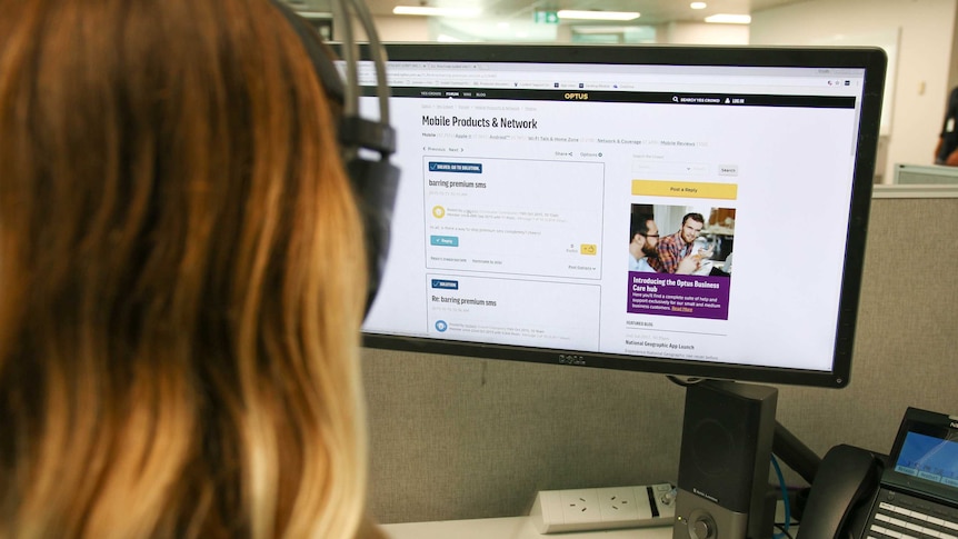 Woman sits in an office with headphones on looking at an Optus webpage