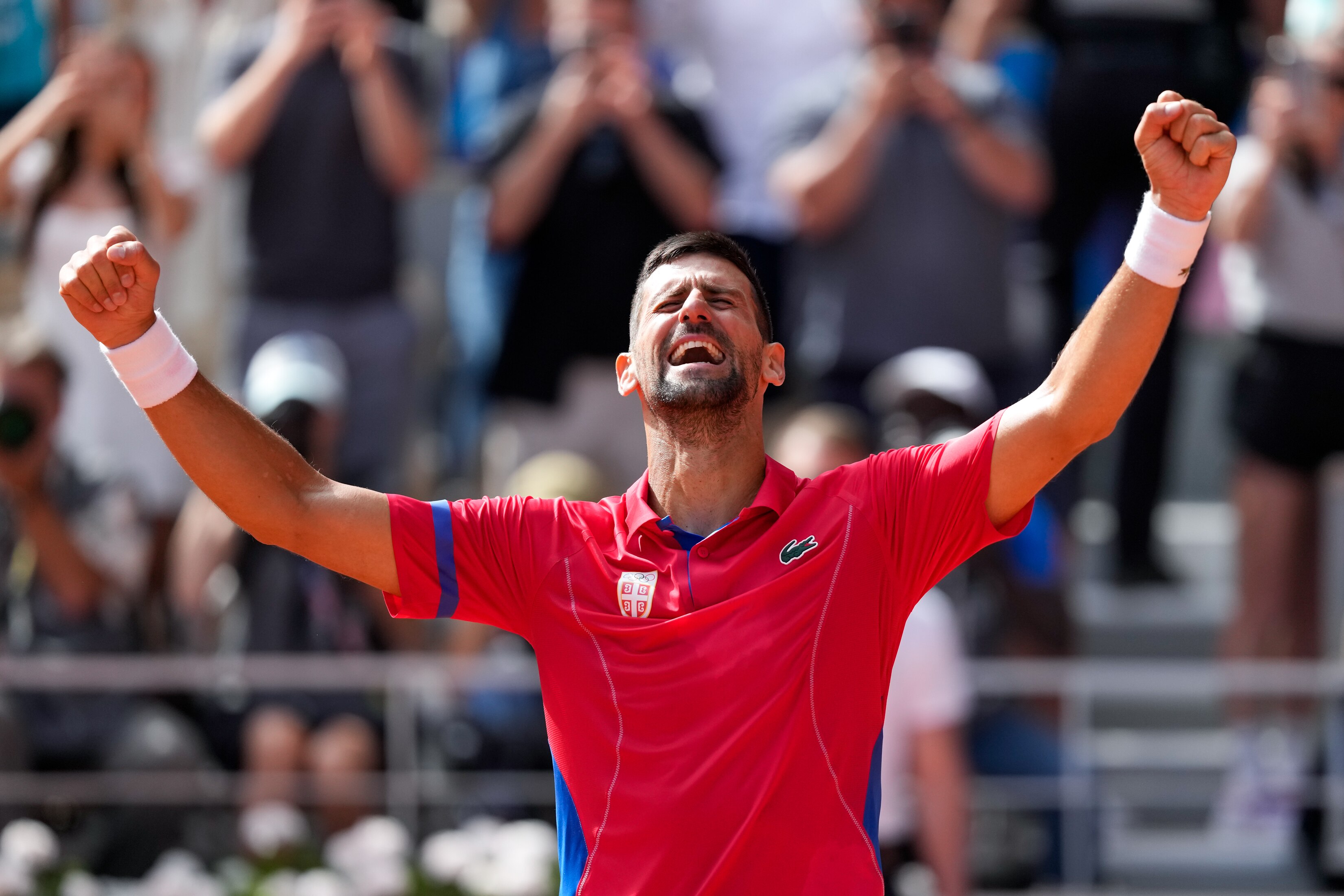 Novak Djokovic celebrates a win with his hands in the air and his eyes closed as he cheers happily