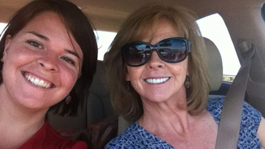 A woman with brown hair smiles in a car next to an older woman with dark blonde hair and sunglasses in a selfie.