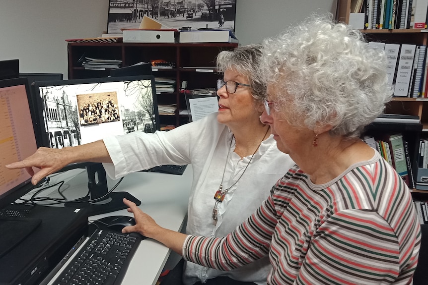 Two women scanning the Colac & District Family History Group database on a computer. One woman is pointing at the screen.