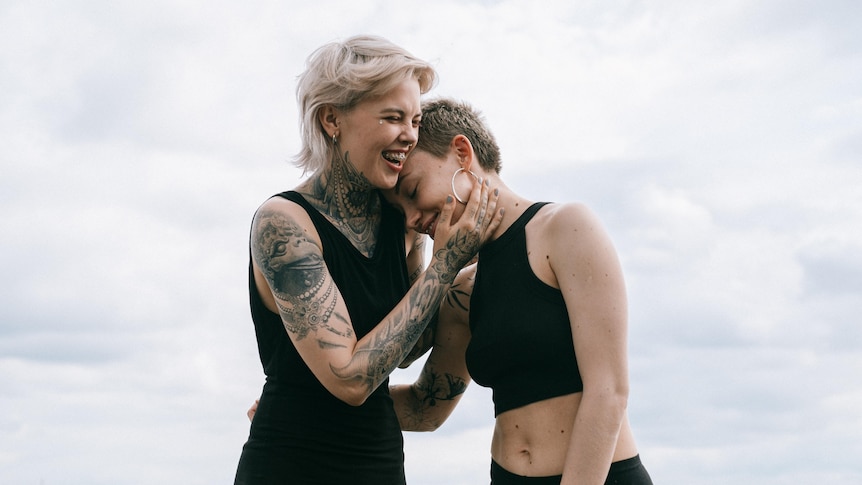 Two women smiling and embracing outside, finding ways to support each other during hard times.