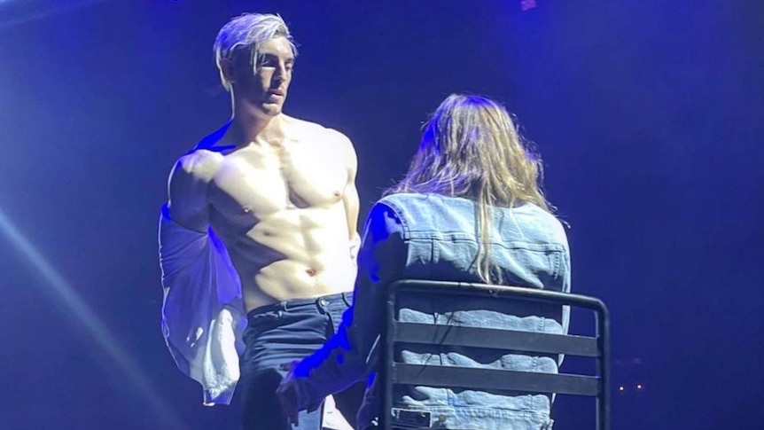 A shirtless man standing in front of a seated woman. 