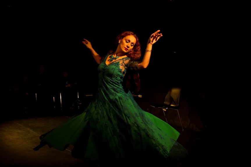 A woman with red hair dances in a green dress.