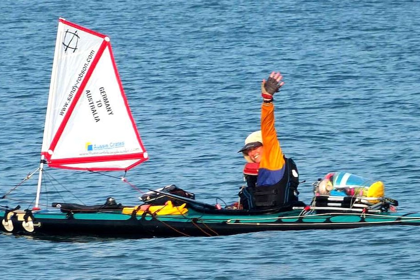 A woman raises her arm in victory as she sits in a kayak.