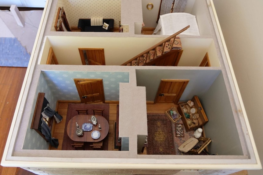 Photograph of a dolls house from above with no roof, four rooms and stairs