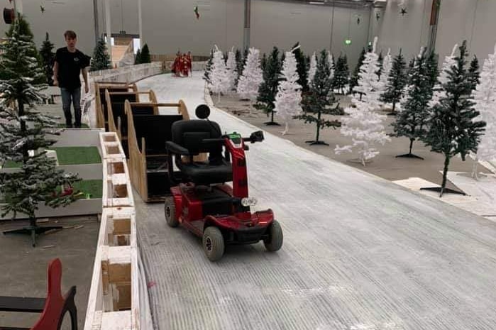 A gopher, dragging wooden slays, in a large warehouse, next to several plastic christmas trees.