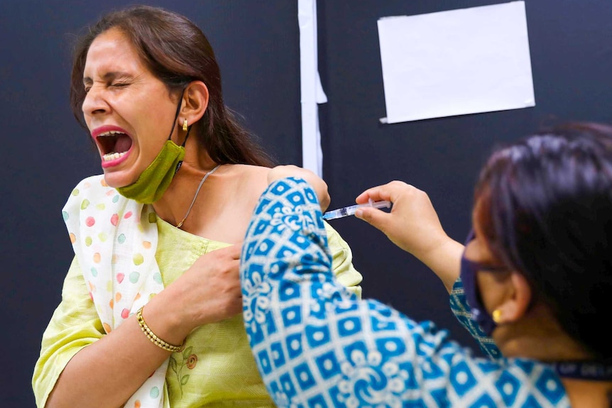 A woman wincing as a nurse holds a needle to her shoulder