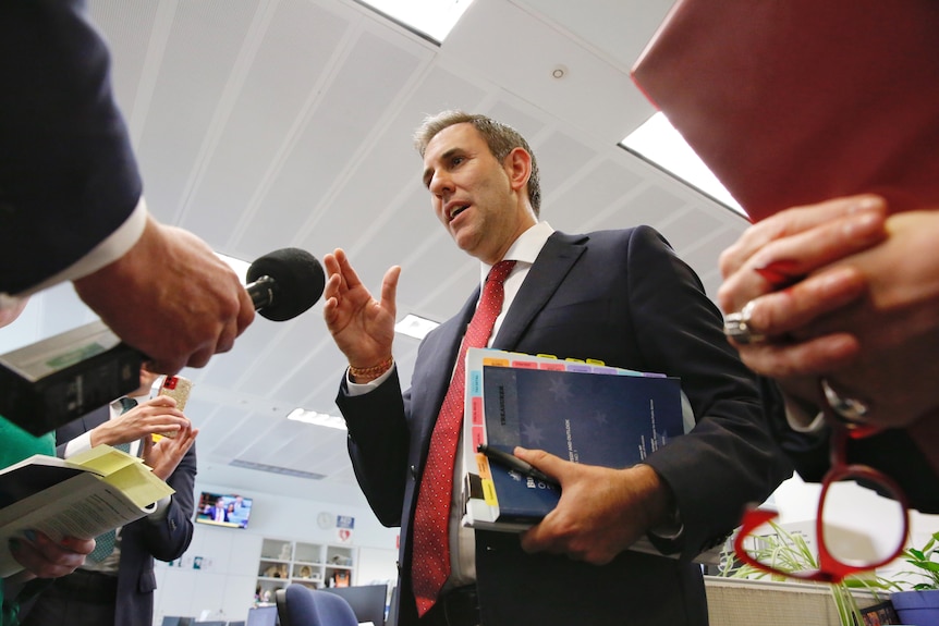 Reporters hold microphones up to Treasurer Jim Chalmers as he holds a stack of budget papers.