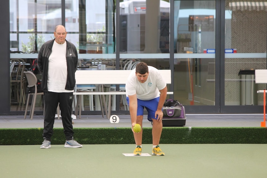 A man prepares to bowl on a bowling green while another man watches on