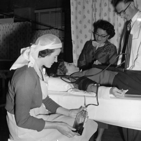 A nurse holding a glass bottle containing a blood donation with the patient in bed beside her.