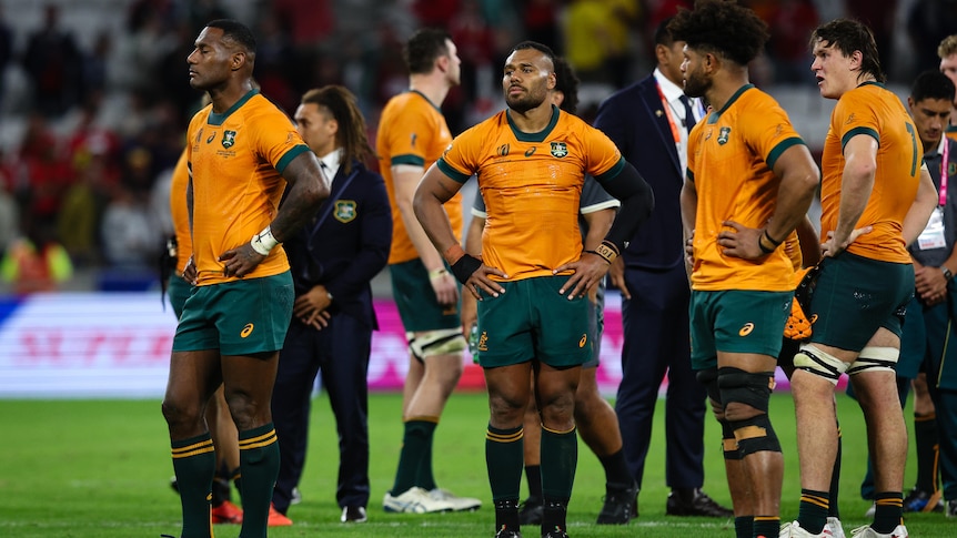 A group of glum-looking Australian rugby union players stand around on the pitch after losing a big game. 