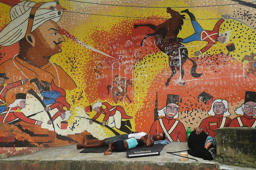 A family sleeps in front of a mural showing Tipu Sultan. It also shows British soldiers being injured.