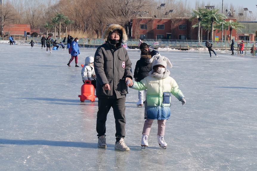 A man holding a child's arm as they skate on ice in a park.